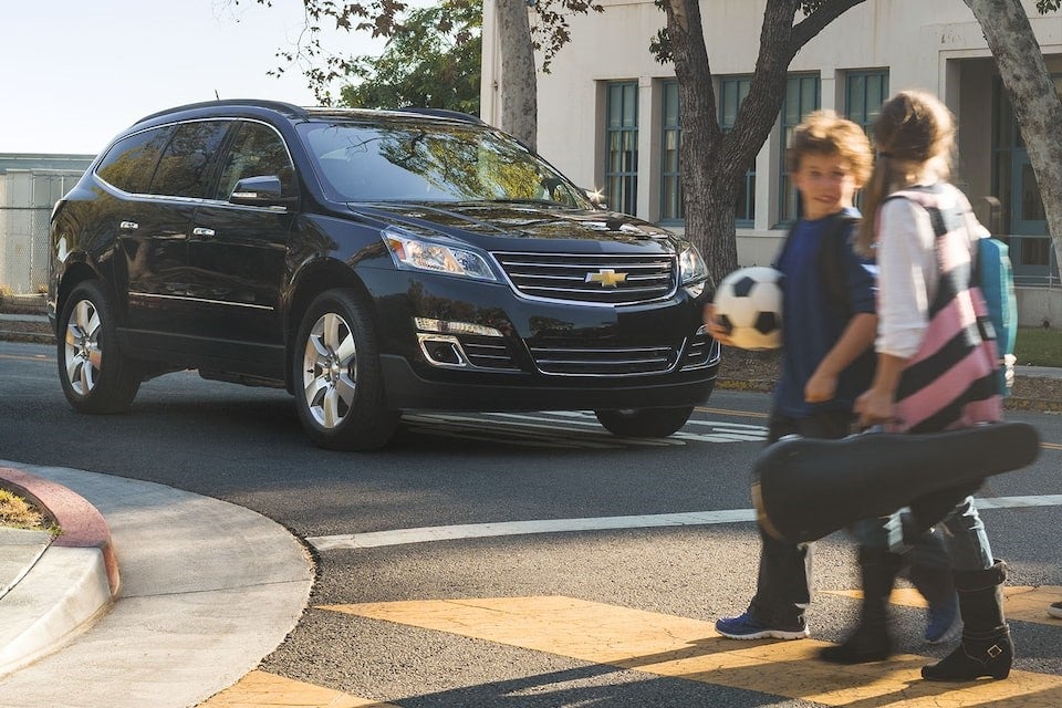 A two kids carring football and game material and crossing a road near by black SUV